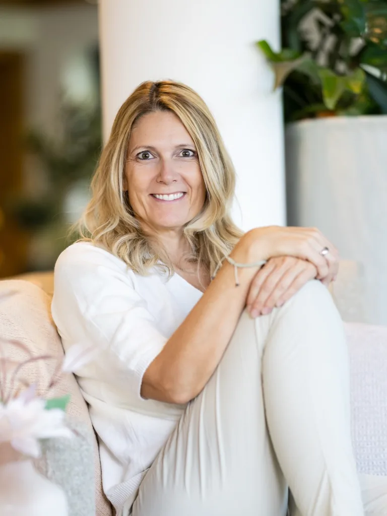 Heidi Kaiser sitzt lächelnd auf dem Sofa, die Hände auf dem angewinkelten Knie